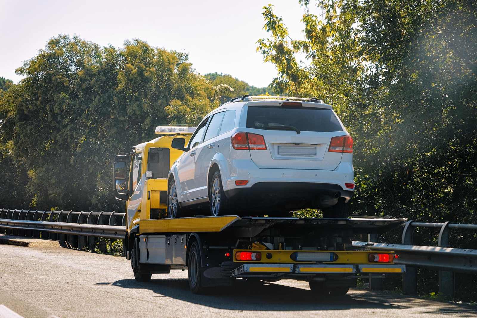 Carro attrezzi giallo che trasporta un SUV bianco su strada a scorrimento veloce